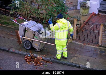 Road Escoba barriendo las hojas de la canaleta, Holloway Islington, Londres, Inglaterra Foto de stock