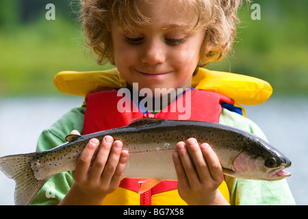 Un joven pescador orgullosamente examina las truchas arco iris que capturados en el lago ingenio h su nueva caña de pescar en una noche de verano.