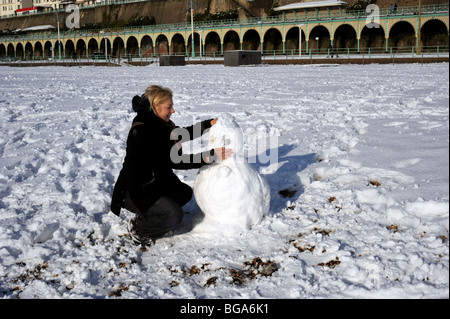 Una mujer construye un muñeco de nieve en la playa de Brighton Foto de stock