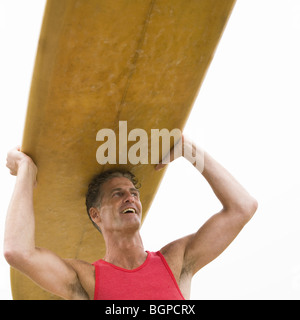 Ángulo de visión baja de un hombre maduro, llevando una tabla de surf y sonriente