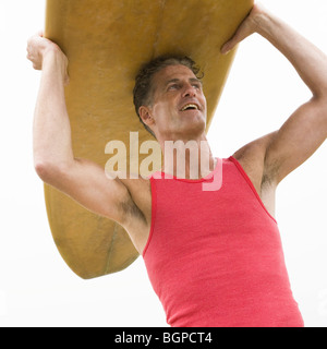 Ángulo de visión baja de un hombre maduro, llevando una tabla de surf y sonriente