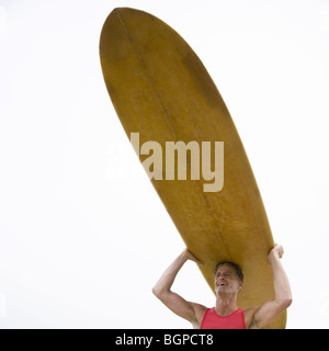 Ángulo de visión baja de un hombre maduro, llevando una tabla de surf