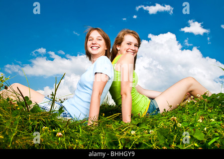 Dos jóvenes adolescente amigos sentados espalda con espalda en verano meadow