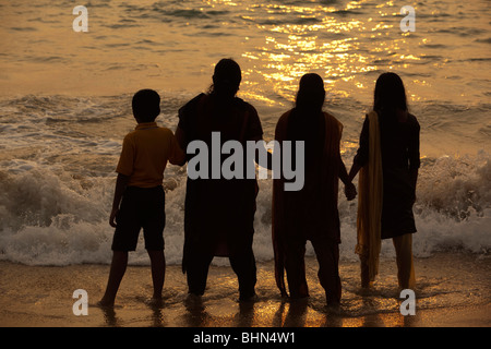India, Kerala, Kovalam, Hawah (Eve) Playa familia india, tomados de la mano en la orilla del mar al atardecer Foto de stock