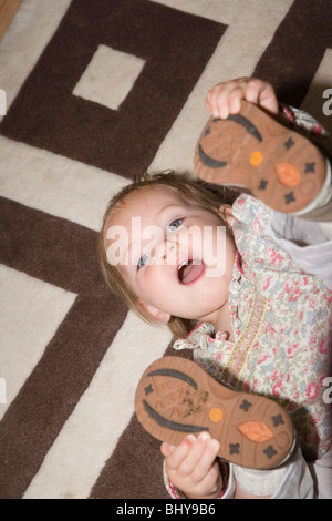 Niña de 17 meses está mintiendo y jugando sobre la alfombra en casa. Foto de stock
