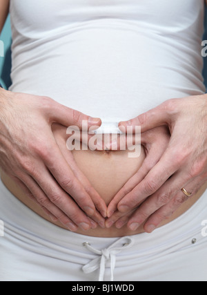 Licencia disponible en MaximImages.com - Mujer embarazada y su marido haciendo un corazón con sus manos sobre su vientre Foto de stock
