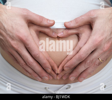 Licencia disponible en MaximImages.com - Mujer embarazada y su marido haciendo un corazón con sus manos sobre su vientre Foto de stock