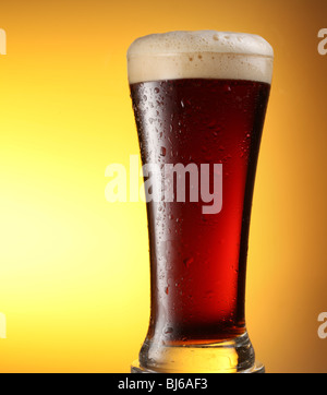 Vaso de cerveza oscura sobre un fondo amarillo