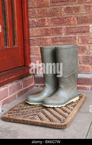 Verde botas Wellington en la alfombrilla de la puerta por fuera de la puerta delantera Foto de stock