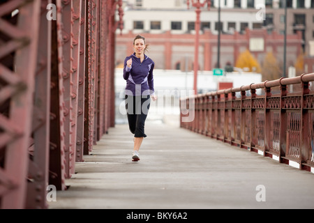 Una prueba de atletismo femenino en una chaqueta de color púrpura que corre a lo largo de un puente en Portland, Oregon.