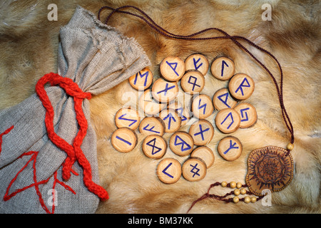 Las runas de madera artesanales con bolsa y amuleto en el fondo de pieles Foto de stock