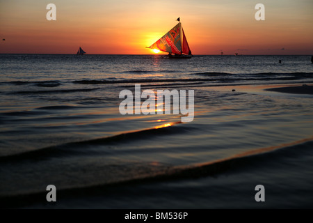 Un bote de vela pasa el atardecer en la Playa Blanca, Boracay, el destino turístico más famoso en Filipinas.