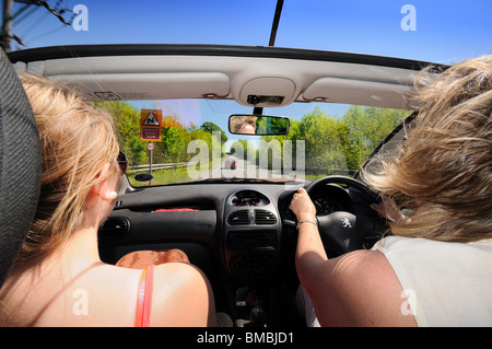Open top coche con conductor y pasajero femenino en carretera abierta