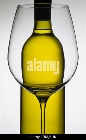 Botella de vino blanco detrás de un vidrio de vino blanco con iluminación trasera, con vistos a través de la botella de vidrio refracta Foto de stock