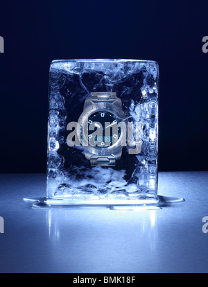 Un bloque congelado de hielo con un reloj de pulsera congeladas por dentro sobre una superficie metálica Foto de stock