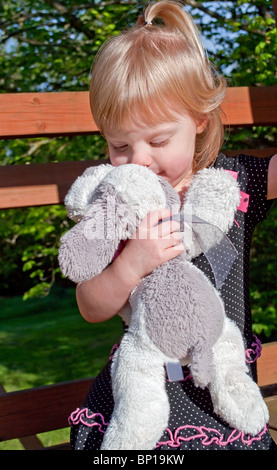 Este precioso shot imagen muestra una niña de 2 años del Cáucaso besar su peluche favorito, un perro de peluche blanco y gris. Foto de stock