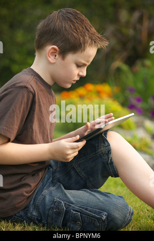 Un muchacho de 10 años de edad utilizando un iPad en el jardín Foto de stock