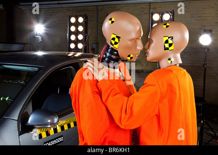 Dos Crash test dummies junto a un coche en un laboratorio de pruebas de choque acerca de beso Foto de stock