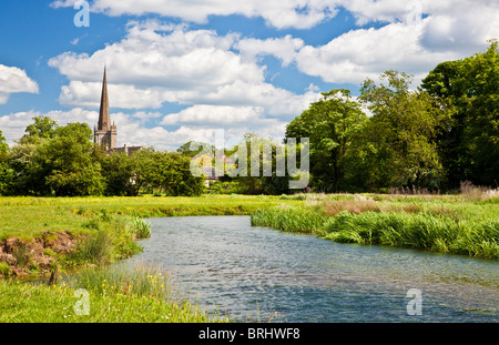 Vista de verano a través de pradera y río Windrush a San Juan Bautista, Iglesia en la ciudad de Cotswold de Burford, Oxfordshire, Inglaterra, Reino Unido.