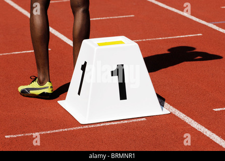 Las piernas de un velocista masculino junto al bloque de partida número uno de la pista de atletismo fuera Foto de stock