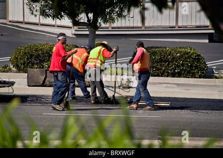 Los obreros hispanos vistiendo chalecos de seguridad de alta visibilidad propagación lechada caliente sobre el pavimento en una calle de Laguna Niguel, CA Foto de stock