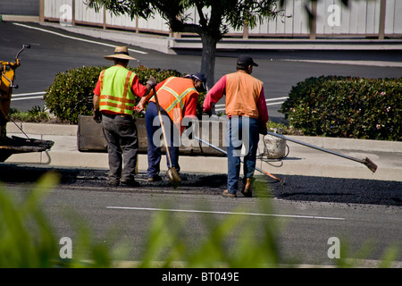 Los obreros hispanos vistiendo chalecos de seguridad de alta visibilidad propagación lechada caliente sobre el pavimento en una calle de Laguna Niguel, CA Foto de stock