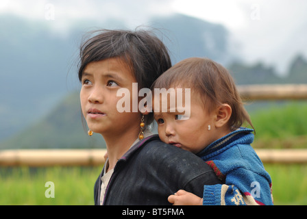 Dao Tribal Black niña cargando un hermano bebé cerca de Sapa, Vietnam Foto de stock
