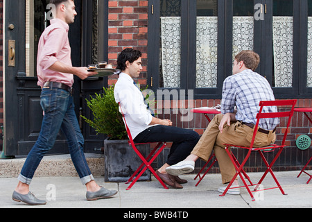 Camarero trayendo café a los hombres fuera de cafe