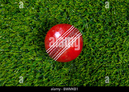 Foto de una bola de cricket de cuero rojo con costuras sobre el césped