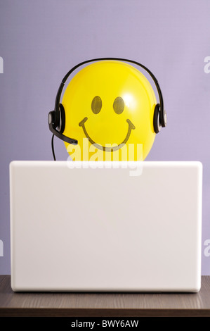 Globo de cara sonriente con auriculares en el ordenador portátil Foto de stock