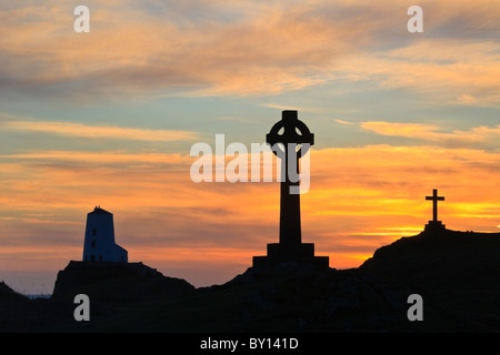 St Dwynwen cruz celta y Twr Mawr faro en la silueta de la isla Llanddwyn al atardecer / Puesta de sol. Isla de Anglesey al norte de Gales, Reino Unido Gran Bretaña