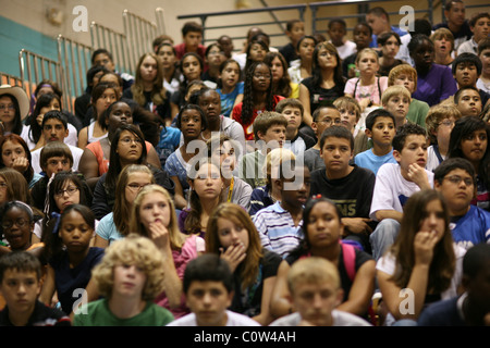 Los estudiantes de escuela intermedia sentarse en gradas en el gimnasio de la escuela para ver la diversidad rendimiento diario durante el montaje Foto de stock