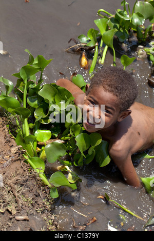 Boy ayudar a quitar invasiva de bora (Eichhornia crassipes), laguna de un pueblo. Madagascar. Foto de stock