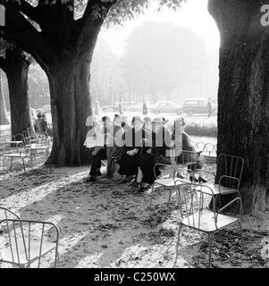 Francia,1950. Durante el invierno y fuera en una parte, un hombre lee su periódico con otros parisinos sentados juntos en un banco en París.