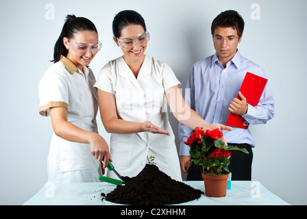Tres biólogos que trabajan en el laboratorio ,ellos sonriendo y uno de mujeres que muestran a una planta en patchwork Foto de stock