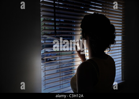 Mujer mirando aunque la persiana de una ventana en una oscura calle vacía.