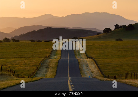 Luz del amanecer dorado más larga recta de dos carriles y rolling hills country road en primavera, Santa Ynez Valley, California. Foto de stock