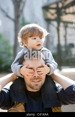 Padre de un hijo pequeño llevando sobre sus hombros, hijo del padre que cubre los ojos con sus manos