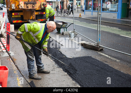 Los obreros la reparación de carreteras dañadas por el tiempo y el tráfico, Glasgow, Escocia Foto de stock