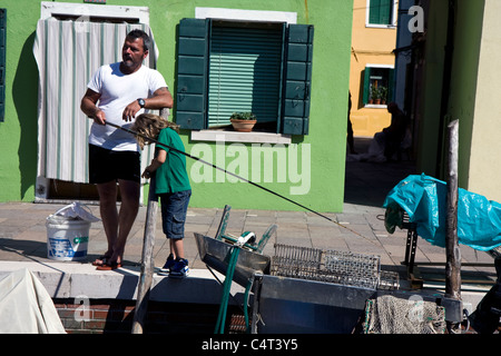 El hombre y el niño la pesca en un canal en la ciudad de Burano en Italia, junto a Venecia