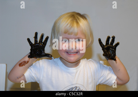 Close-up retrato de niña sonriente con pintura negra en sus manos