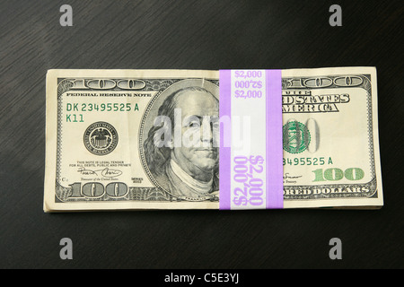 Dos mil dólares en billetes de 100 en una mesa de madera oscura Foto de stock