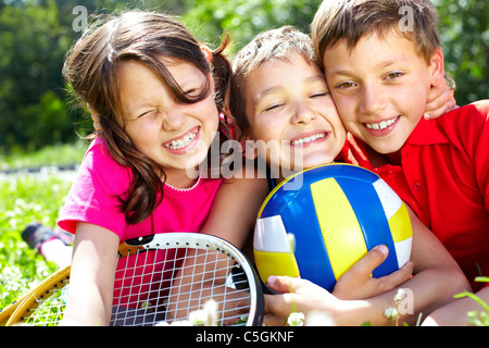 Tres niños con equipo deportivo abrazando, mirando a la cámara y sonriendo