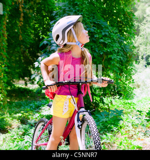 Los niños chica en bicicleta en el bosque exterior sonriente con casco