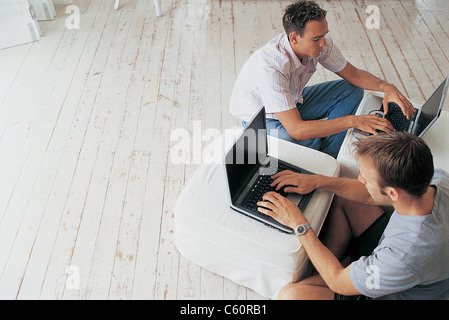 Los hombres que usan computadoras portátiles en la sala de estar Foto de stock