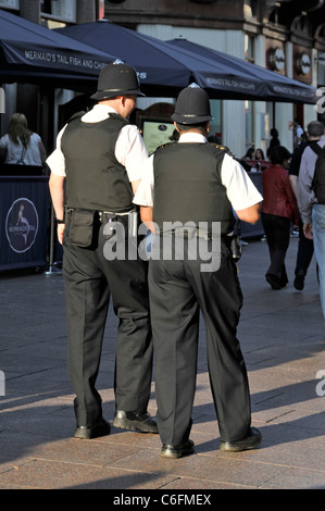 London street scene vista posterior de dos funcionarios de la Policía Metropolitana en uniforme sobre un beat patrol en el verano soleado de Leicester Square West End Inglaterra Foto de stock