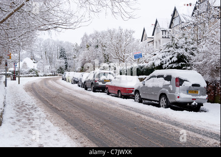 Winter Village Street (pistas de coches en una tranquila carretera cubierta de nieve, coches estacionados, huellas en pavimento desierto) - Burley en Wharfedale, Inglaterra, GB, Reino Unido. Foto de stock