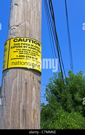 Señal de precaución de National Grid en madera palo de energía eléctrica en la ciudad de Nueva York borough street, EE.UU. Foto de stock