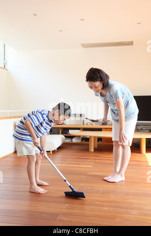 La madre y el niño del piso de barrido con escoba y pala para recoger