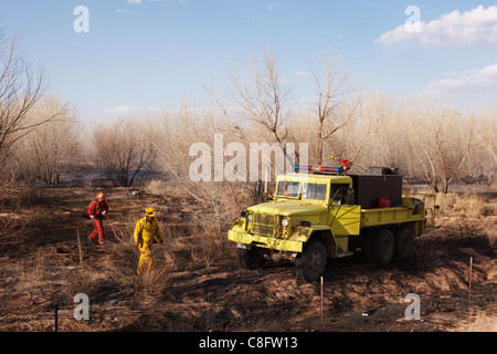 Camión de bomberos y rural en Nuevo México diluir los puntos calientes de un incendio de matorrales. Foto de stock
